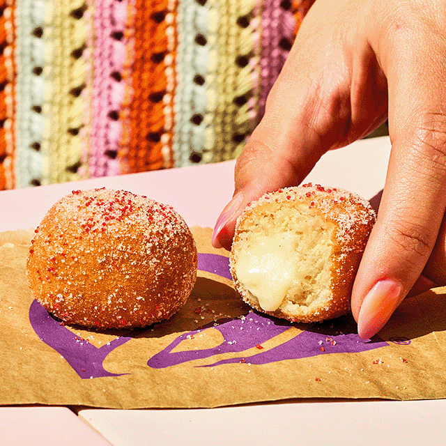 A hand holding a new Strawberry Cinnabon Delight® with a bite taken out, featuring the signature cream-cheese frosting filling, next to another untouched Strawberry Cinnabon Delight®.