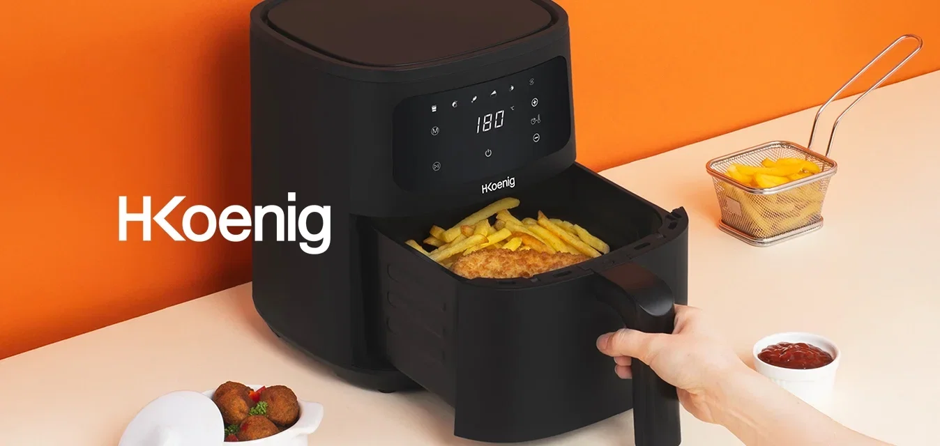 Tirer à la main un panier contenant des frites cuites et des aliments panés d'une friteuse à air numérique noire sur un comptoir beige avec un mur orange.