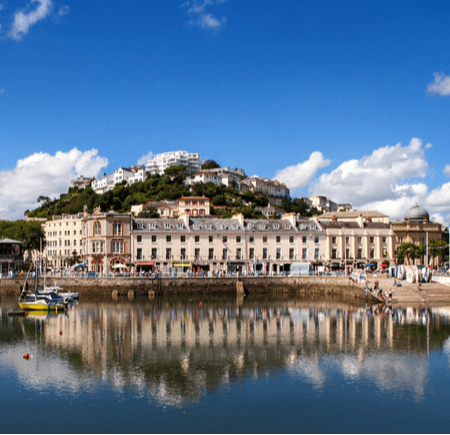 Coastal view of a town with buildings reflecting in the water under a blue sky with clouds.