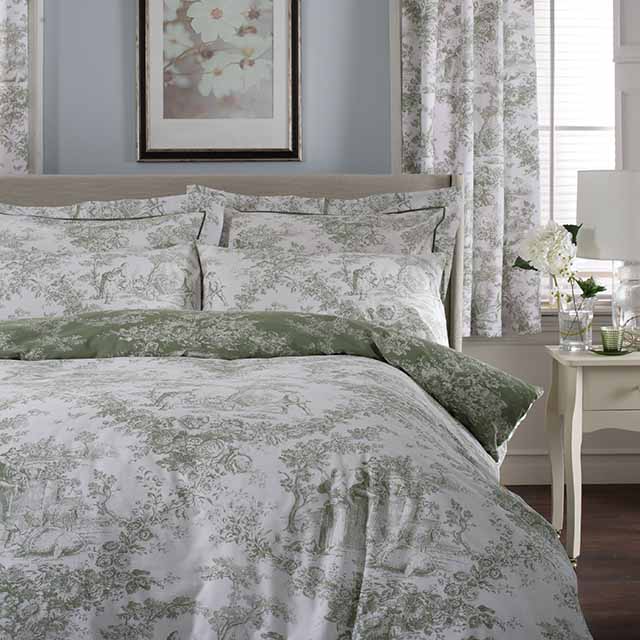 Elegant bedroom with floral-patterned bedding and curtains, framed artwork, and a bedside table with a lamp and flowers.