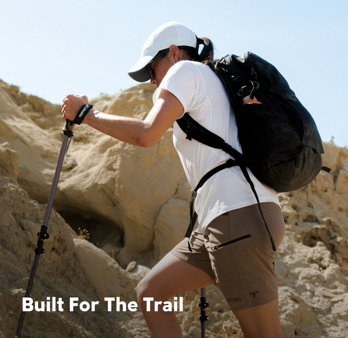 A woman hiking up rocks against a blue sky with text: Built For The Trail