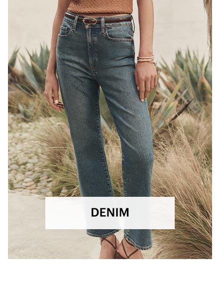 Woman wearing medium wash high rise straight leg jeans, posed outdoors in front of plants. Shop women's denim.