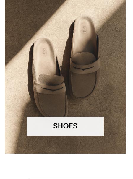 Pair of taupe closed-toe slide loafers on top of a sunlit stone surface. Shop men's shoes.
