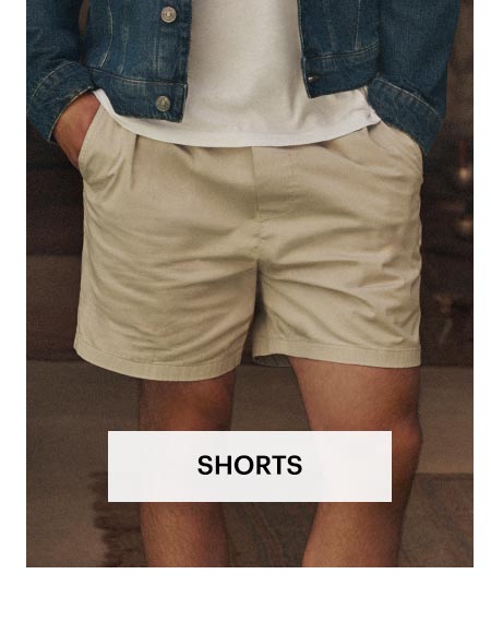 Man wearing a pair of beige cotton shorts in an outdoor area. Shop men's shorts.