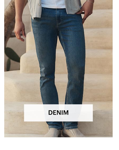 Man wearing a pair of dark wash slim fit jeans in front of a sunlit stone staircase. Shop men's denim.