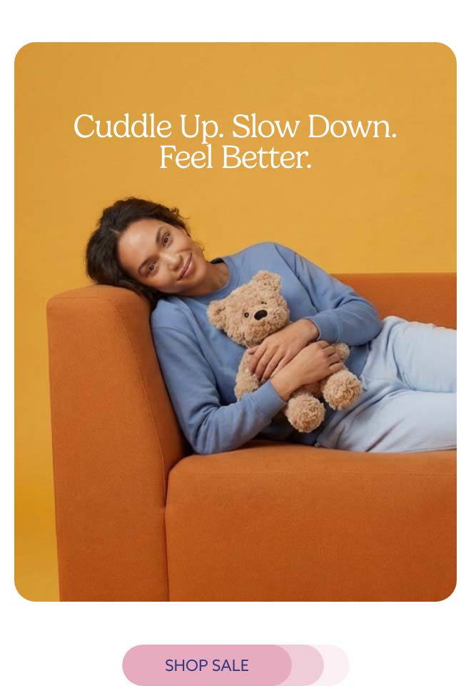 A woman relaxing on a couch with Brown Curly Bear Warmies. Shop Sale.