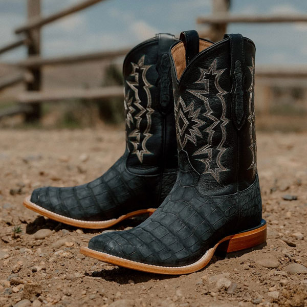 Tony Lama boot sitting on dirt by a fence.