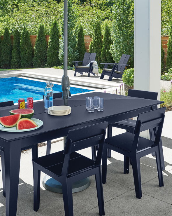 Aspen outdoor dining table in navy with matching chairs beside a pool with watermelon and drinks.