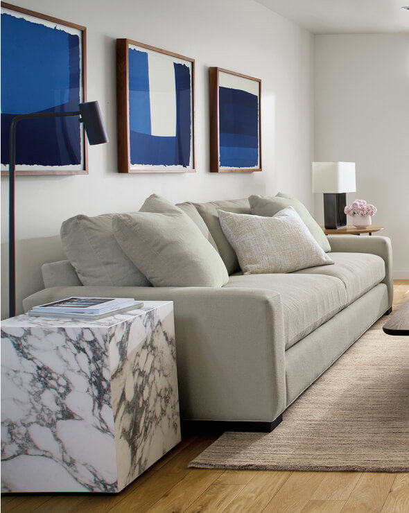 Metro sofa in grey fabric with large cushions styled with a marbled side table and framed blue art.