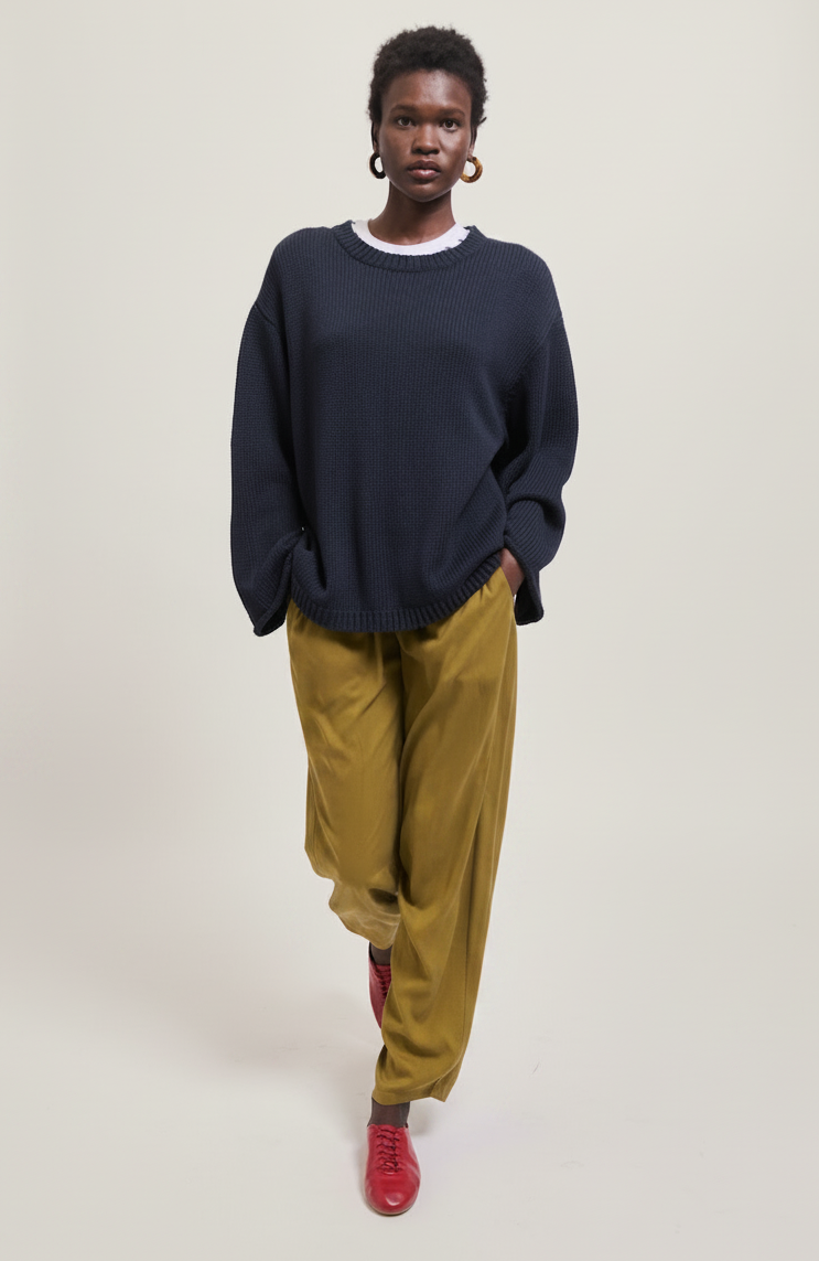 A woman in a navy sweater and olive pants walks forward, wearing red shoes.