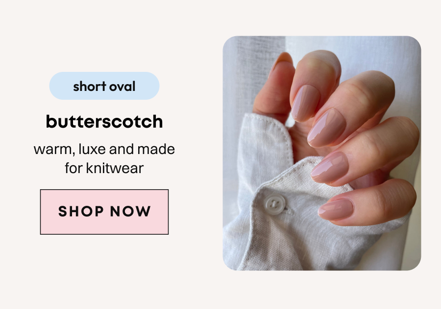 Hand holding white cardigan displaying butterscotch shade press-on nails in peachy nude tone