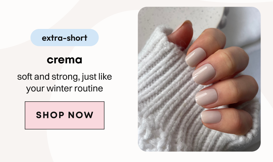 Hand in white ribbed sweater displaying crema shade press-on nails in soft beige tone