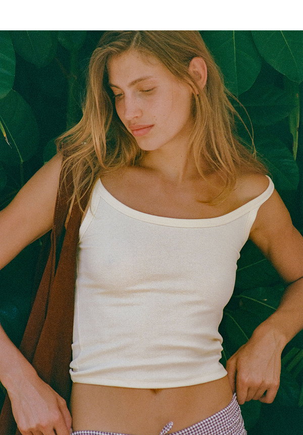 Woman wearing white ribbed tank top against green backdrop