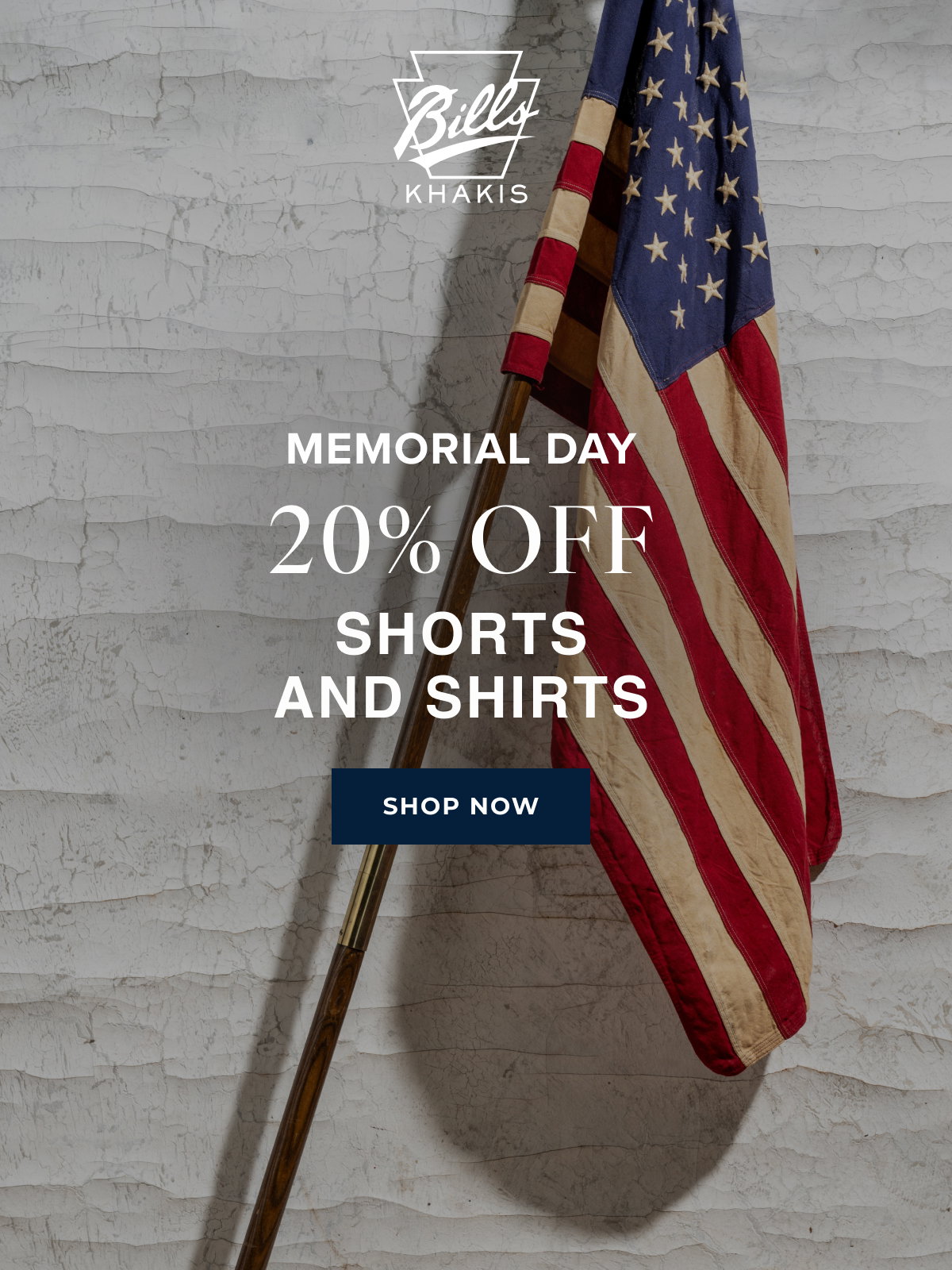A background photo shows an american flag on a pole leaning against a white, industrial wall. The Bills Khakis logo overlays the photo with text that reads: Memorial Day | 20% Off | Shorts and Shirts | Shop Now