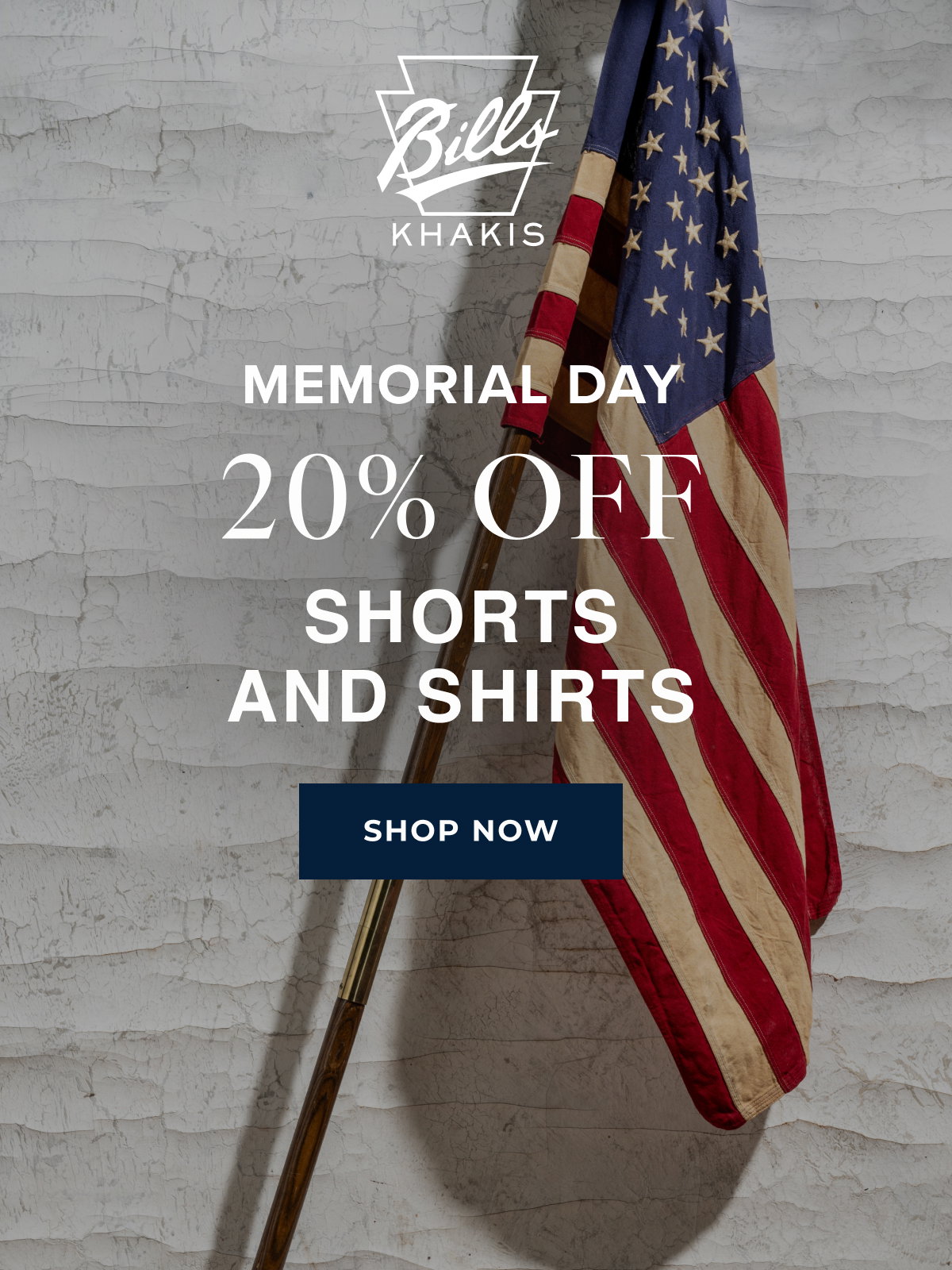 A background photo shows an american flag on a pole leaning against a white, industrial wall. The Bills Khakis logo overlays the photo with text that reads: Memorial Day | 20% Off | Shorts and Shirts | Shop Now