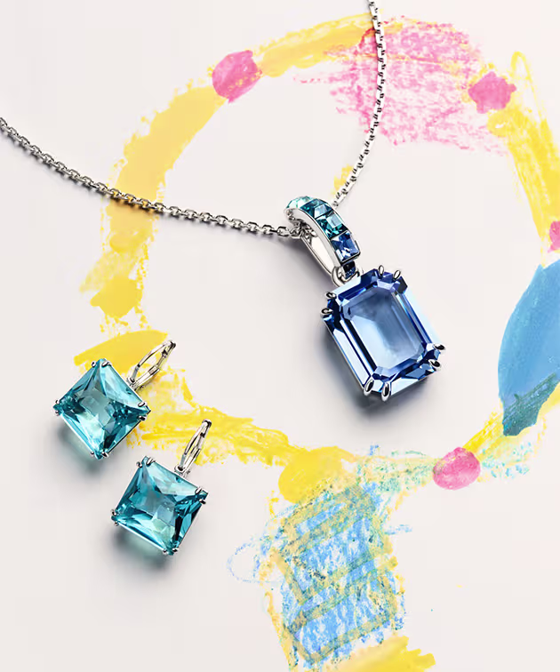 Pendentif et boucles d’oreilles bleus Millenia, posés sur un dessin d’enfant