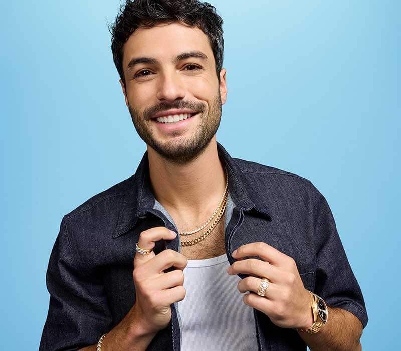 Smiling male model wearing thick yellow gold chains,  rings, bracelets & black-dial watch.