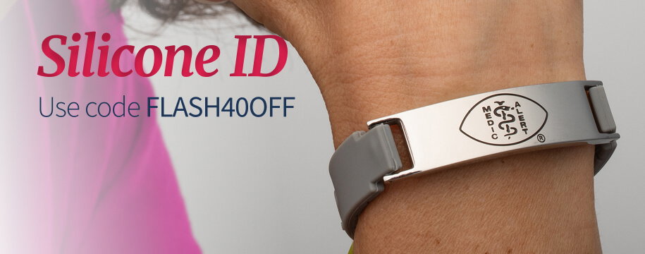 Close-up of a person's wrist wearing a sleek medical ID bracelet featuring a gray silicone band and a rectangular, polished silver tag. The silver tag has an engraved Caduceus logo. Dark red text in the top corner reads 'Silicone ID. Use code FLASH40OFF'.