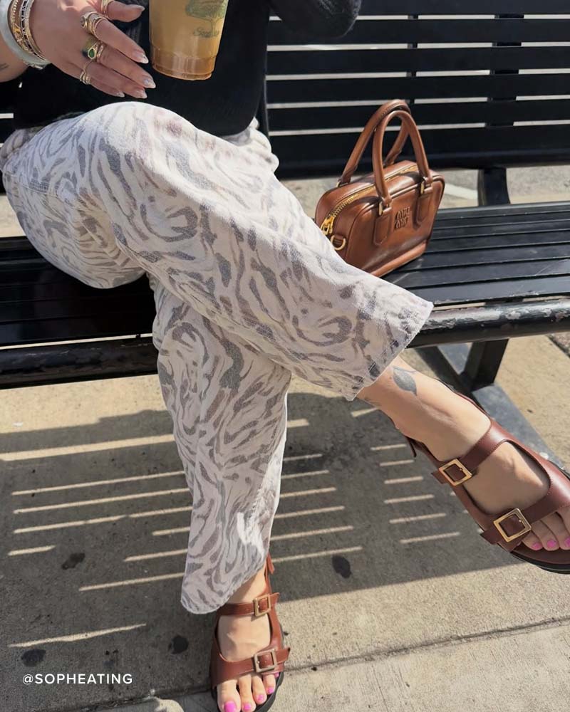 MINDY fisherman sandal in chocolate calf styled with patterned pants, model sitting on a park bench