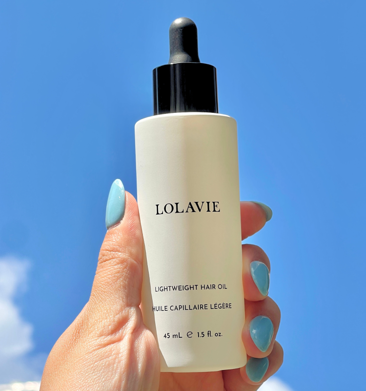 Lightweight Hair Oil in the sky being held by a hand with blue nail polish