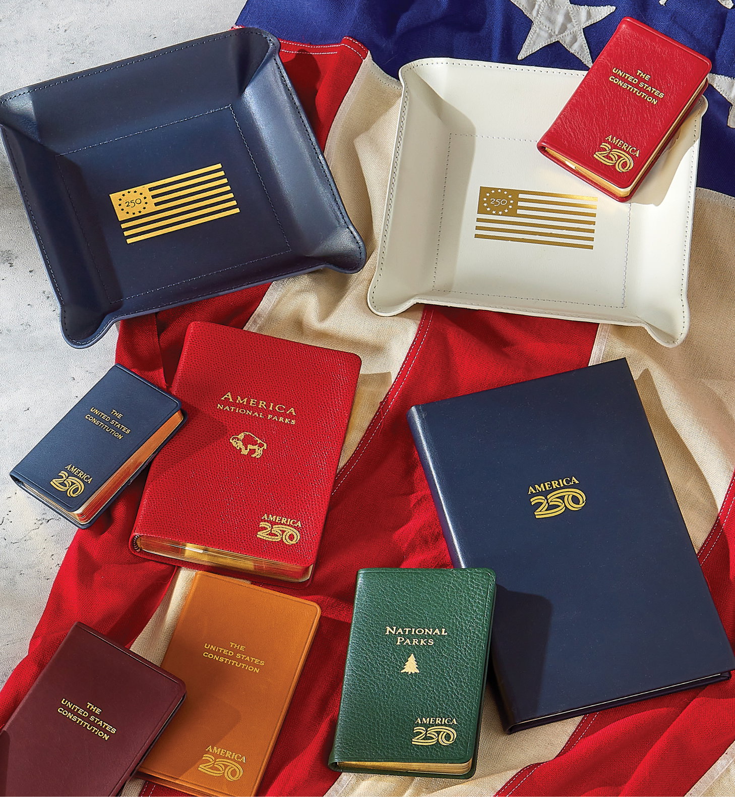 Leather-bound pocket U.S. Constitutions, National Park Atlases, and valet trays all stamped with the America250 logo.