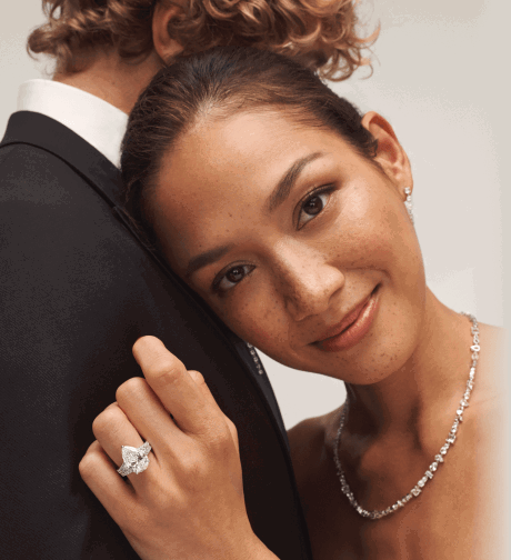 Woman resting on partner’s shoulder wearing pear-shaped diamond ring and diamond necklace.