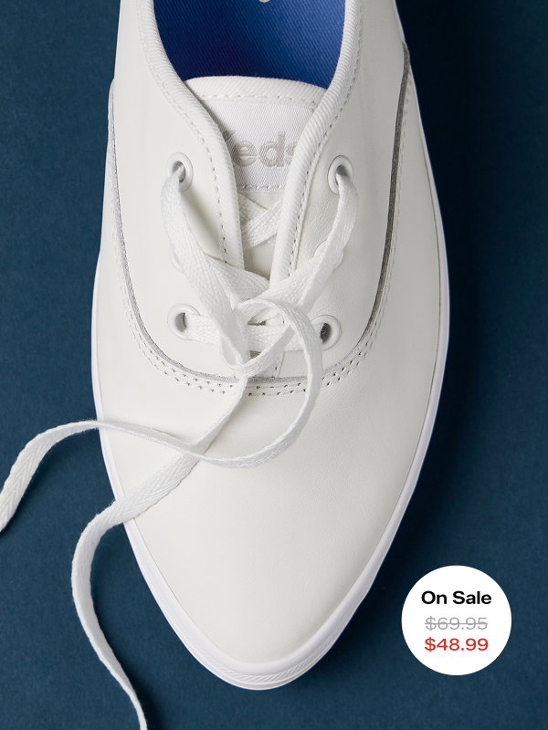 A navy background and a close-up overhead view of the Keds Champion Point Low Leather Lace-Up in white. The style was $69.95 and is on sale for $48.99 for a limited time.