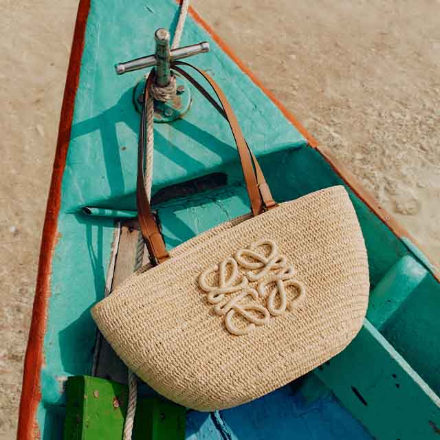 A woven handbag with leather straps rests on a turquoise and red boat next to a rope.