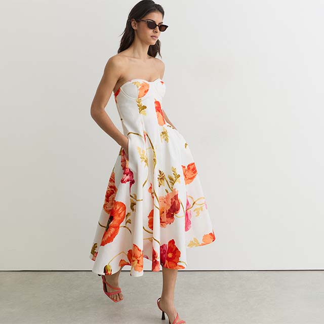 Woman in a strapless floral dress with sunglasses, standing against a plain background.