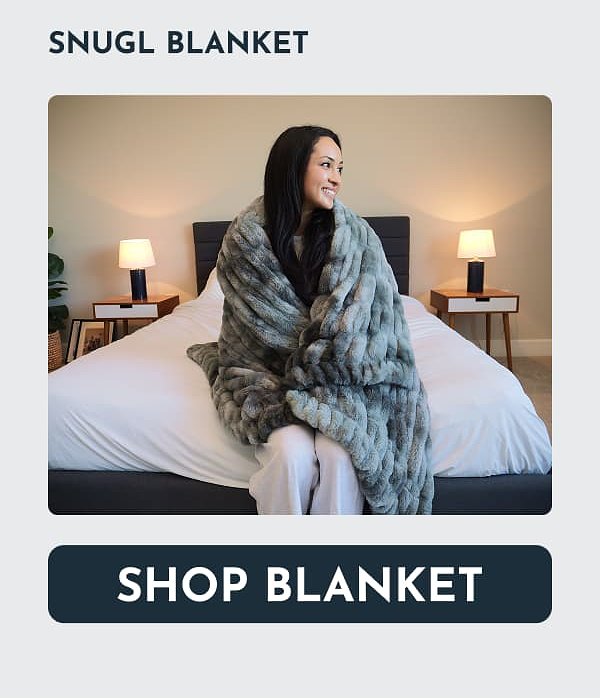 A woman wrapped in a soft blanket sitting on a bed with lamps in the background.