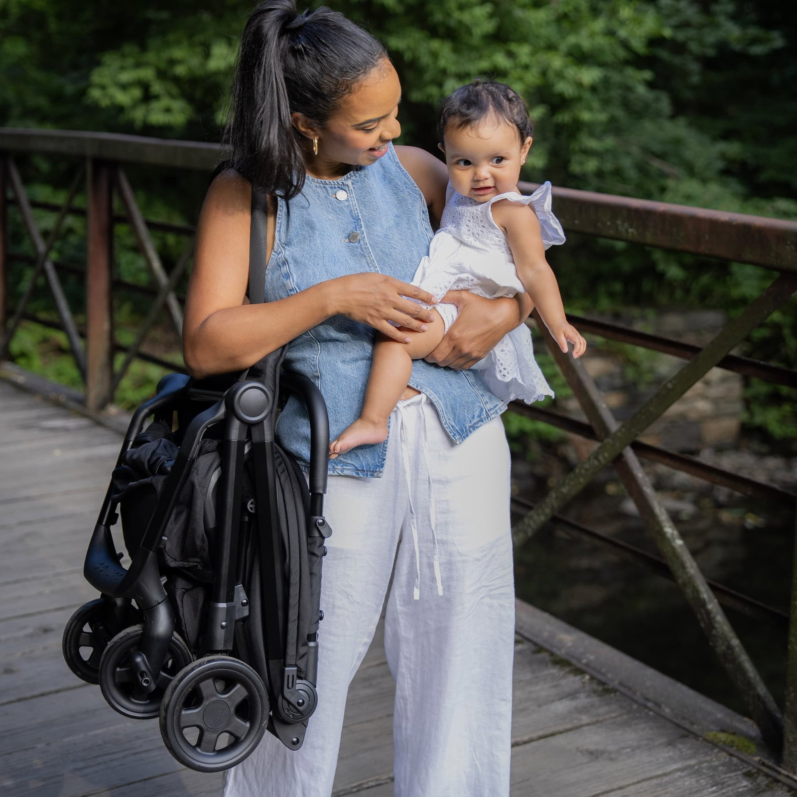 mom holding baby with compact stroller on shoulder