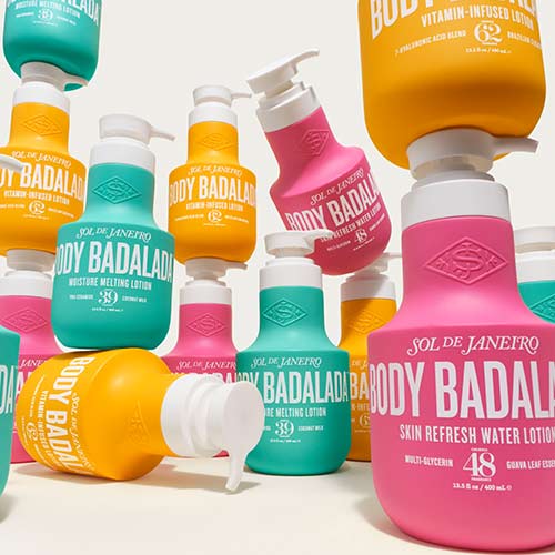 Colourful bottles of Sol de Janeiro Body Badaladas lotions, featuring a mix of yellow, pink, turquoise, and orange colours. Each bottle has a pump dispenser, with labels highlighting different lotion types like 'Vitamin-Infused' and 'Moisture Melting.' The bottles are arranged at varying angles, creating a dynamic composition.