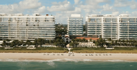 Hero video featuring 4 scenes: 1) Oceanfront view of a hotel along a sandy beach with turquoise water in the foreground. 2) Two girls running outdoors with arms raised and hair billowing with tall buildings and a blue sky in the background. 3) Group of adults sitting together on a beach, laughing and holding drinks. 4) Aerial view of a resort with palm trees and a rectangular pool, surrounded by high-rise buildings.
