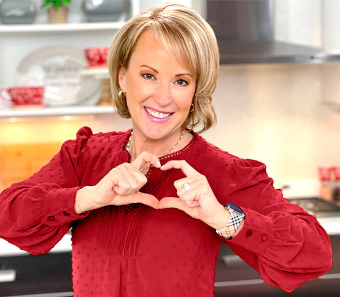 Tara Tesher in her kitchen making a heart shape with hands