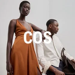 Largo vestido naranja con escote pronunciado y abertura lateral, combinado con una camisa ligera texturizada y pantalones oscuros, acentuado con un bolso marrón.