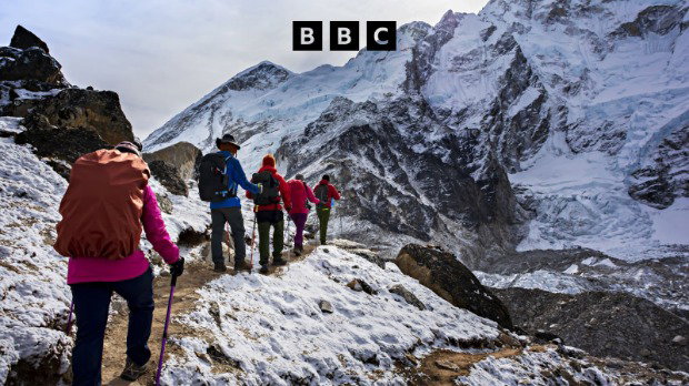 A photograph of a group of climbers on a path on a Himalayan mountain range. A black BBC logo is at the top of the image.