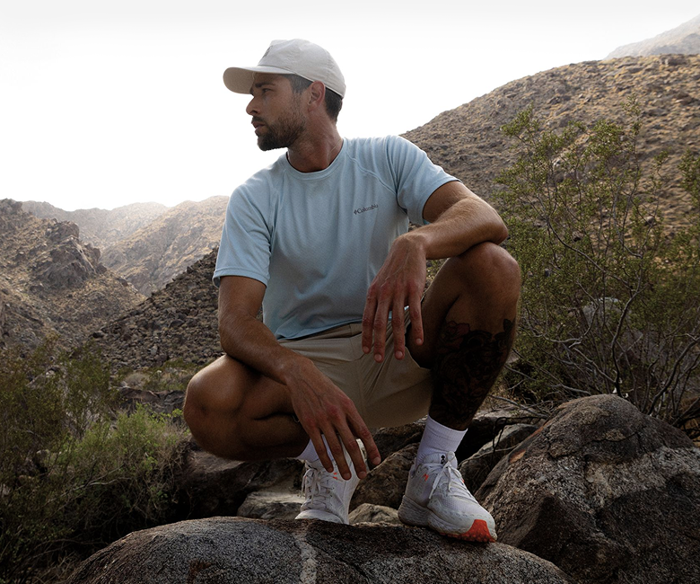 A man kneeling in shorts and a shirt in the desert.