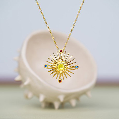 Necklace with pendant inspired by a detail from the Holy Thorn Reliquary, suspended in front of ceramic spiky shape against a pastel background. - Shop Jewellery.