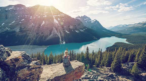 Frau sitzt auf einem Felsvorsprung und schaut auf einen See und Berge des Banff Nationalparks.