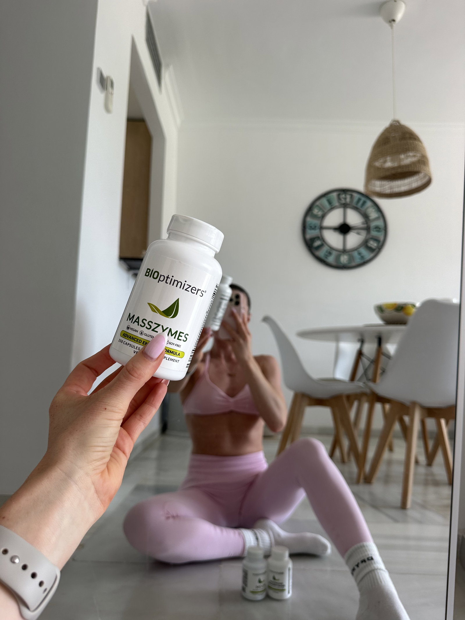 A fitness woman doing a selfie in the mirror holding a BIOptimizers Masszymes bottle 