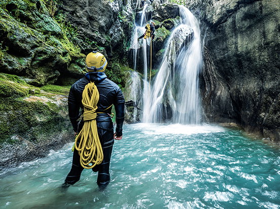 Mann steht in Wasser vor Wasserfall beim Canyoning