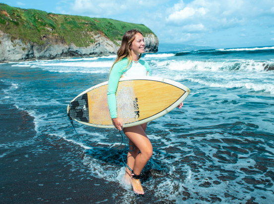 Eine Frau läuft mit ihrem Surfbrett am Wasser entlang.