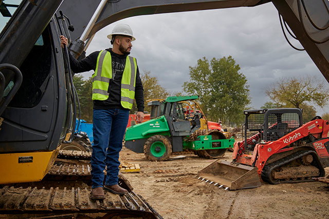 A man wearing Justin Work boots while standing on a tractor.
