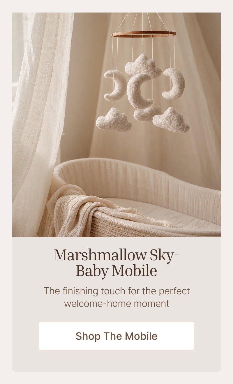 Cream baby mobile hanging above a nursery crib with soft curtains and warm neutral lighting in the background.