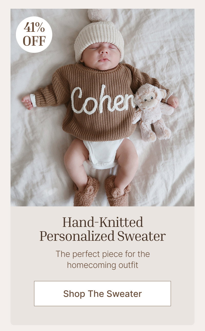Newborn baby lying on a white blanket wearing a personalized brown knit sweater with a small discount badge in the corner.