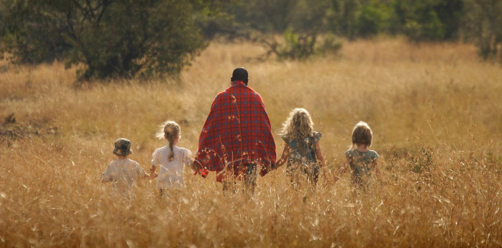 Maasai guide leading children through golden grasslands on safari
