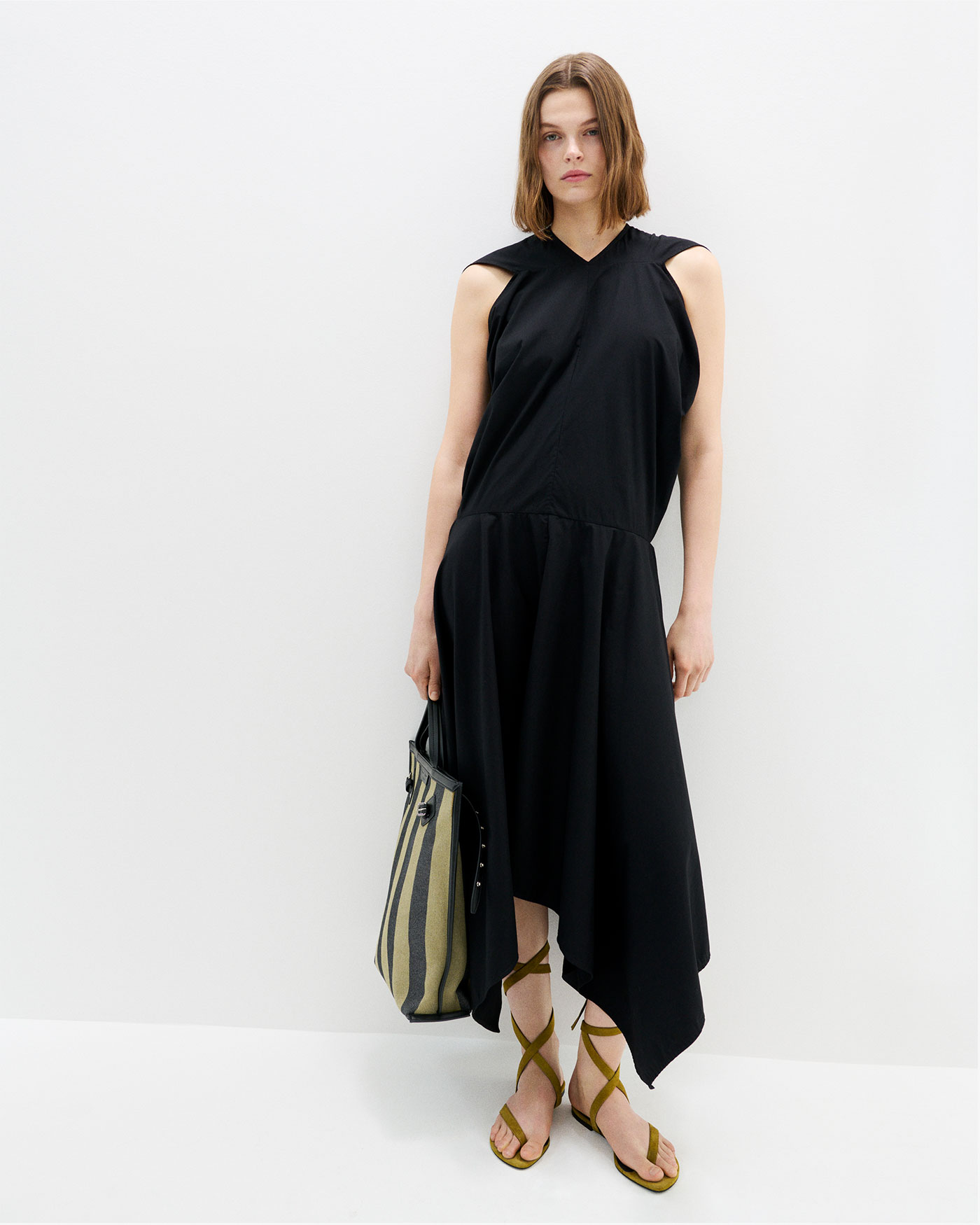Image of model standing against white background wearing Sybella Dress in Classic Cotton Shirting in Black with the North South Days Tote in Striped Canvas in Moss/Black.