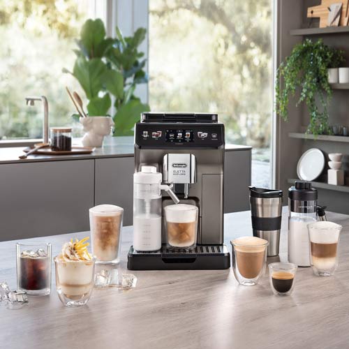 Ninja ice cream maker on a kitchen counter, surrounded by a milkshake in a mason jar, a bowl of vanilla ice cream with chocolate toppings, and bowls of strawberry and chocolate ice cream garnished with strawberries. A plant and kitchen utensils are in the background.