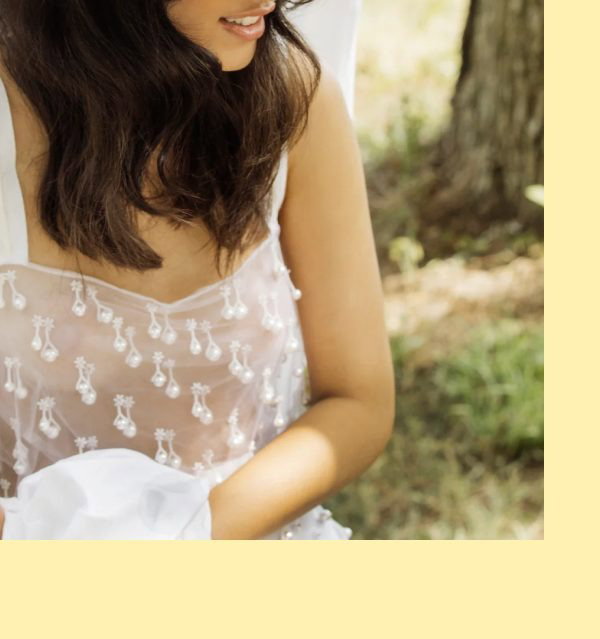 A woman wearing a light top sits outdoors, with a focus on her shoulder and hair.