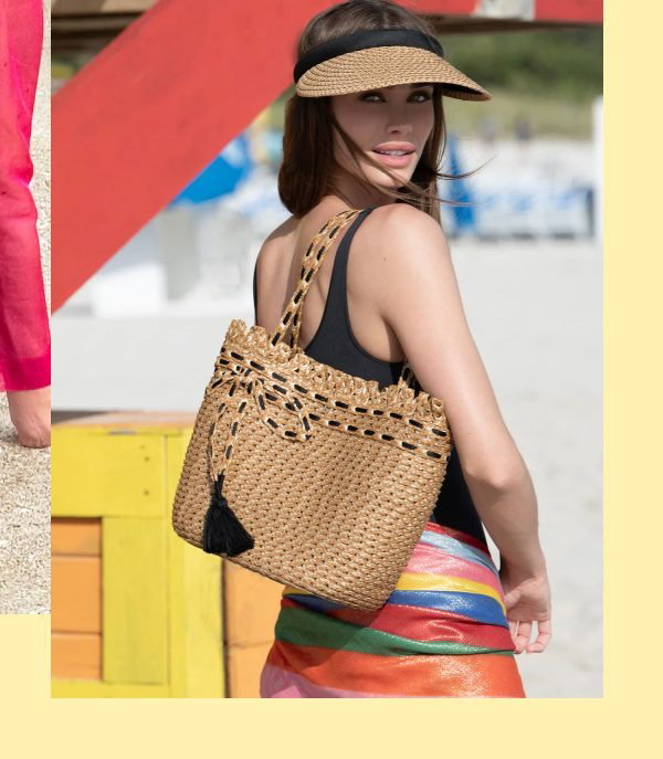 A woman wearing a black top and colorful skirt, holding a woven bag, with a beach background.
